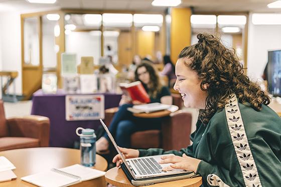 Photo of a female Chatham University student smiling while working at a table in Jennie Mellon King Library.