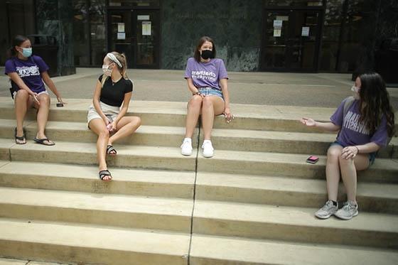 Photo of four Chatham University students, masked, seated socially distanced on the library steps