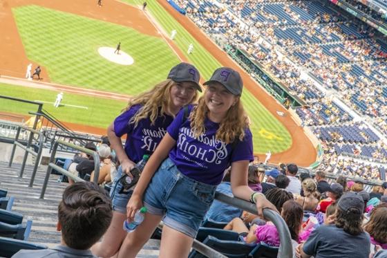  Two female Chatham University choir students in matching purple T-shirts pose together at a Pittsburgh Pirates game.